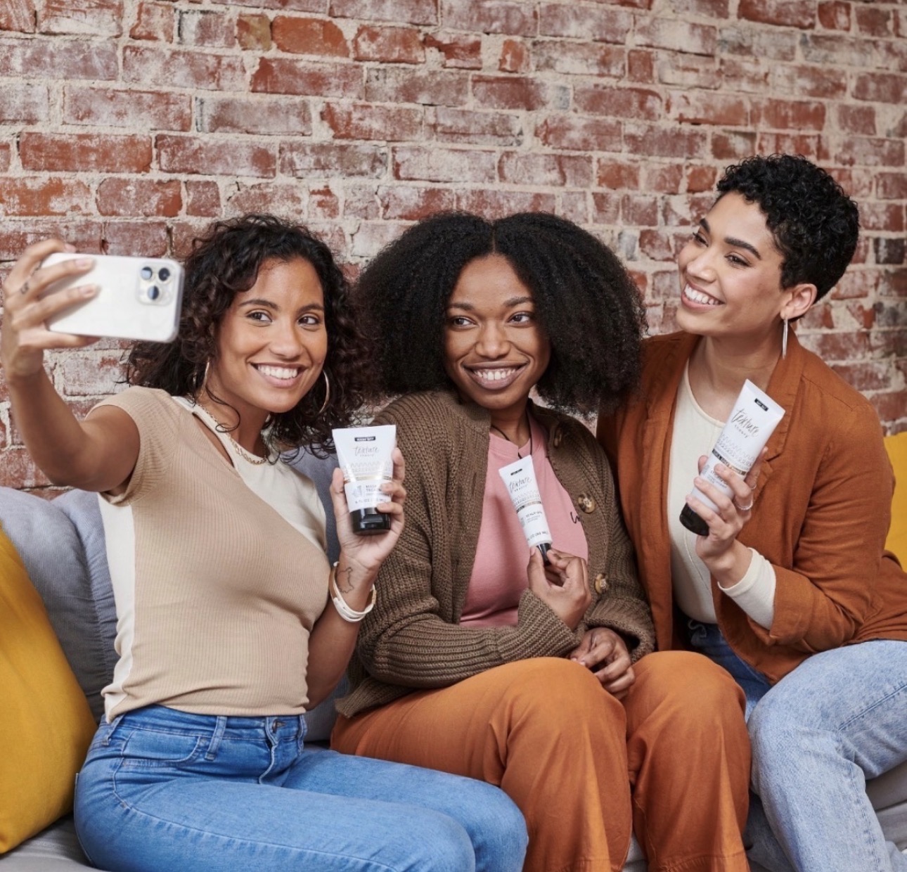 Three women taking a selfie while holding Texture Theory hair care products